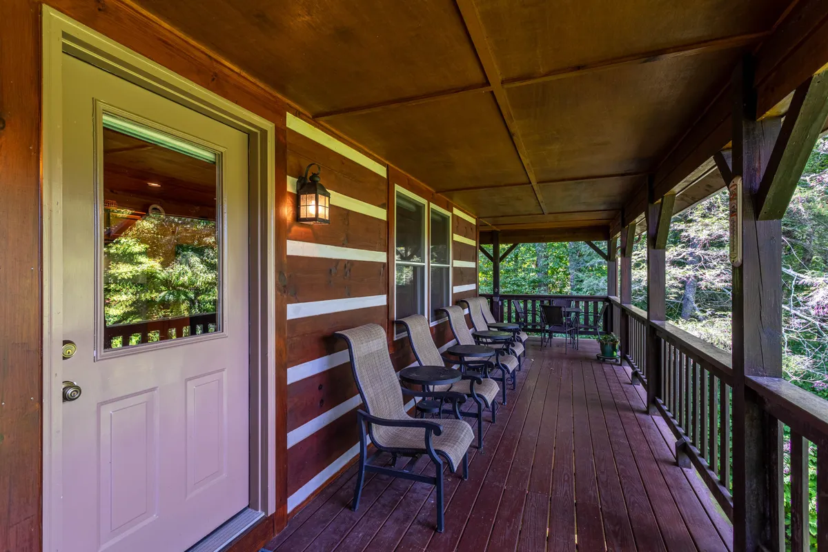 A welcoming view of the cabin’s front porch with a pair of traditional rocking chairs and a sturdy wooden railing, framed by pine trees and inviting outdoor light. The scene suggests moments of peaceful relaxation and conversation immersed in nature.