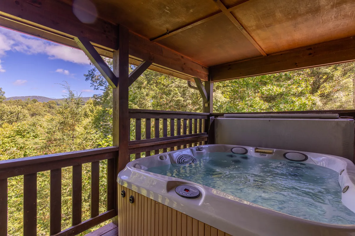 A tranquil setting featuring a hot tub with a panoramic wooden railing overlooking scenic mountain views. The space is perfect for soaking in the outdoors, with hints of nature all around and an atmosphere ideal for both relaxation and stargazing.