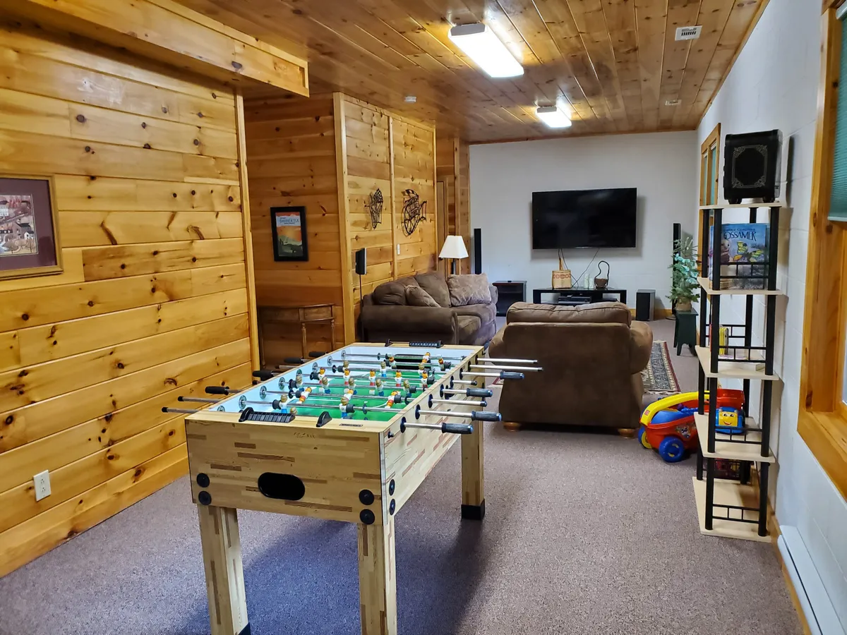 This interior space features a foosball table prominently displayed in the room, with a sofa and television set up for movie viewing. Bookshelves add a casual, lounge-like feel, emphasizing both play and relaxation. The overall mood is playful and relaxed, perfectly in line with a family or friends’ gathering spot for games or movie nights.