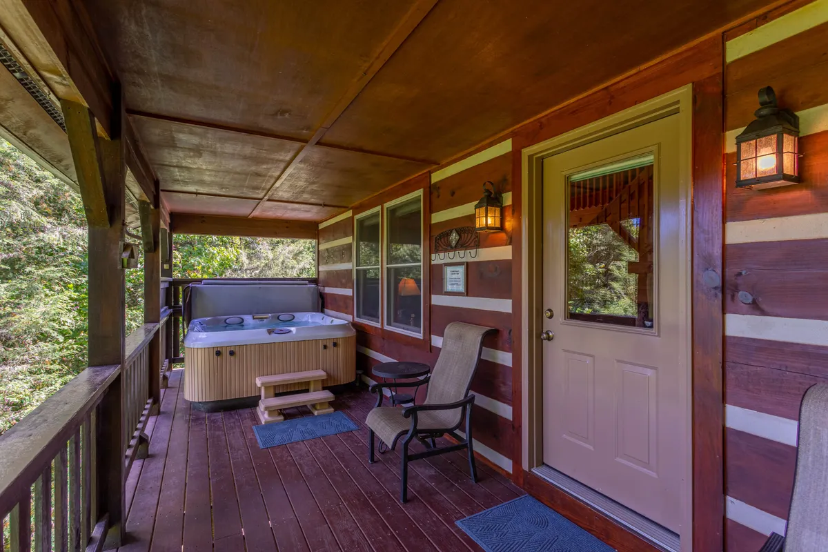 A cozy exterior view of the cabin’s wooden deck featuring a bubbling hot tub, a classic wooden rocking chair, and the surrounding natural landscape. The space is illuminated by gentle natural light, and the scene evokes a sense of relaxation and immersion in nature.