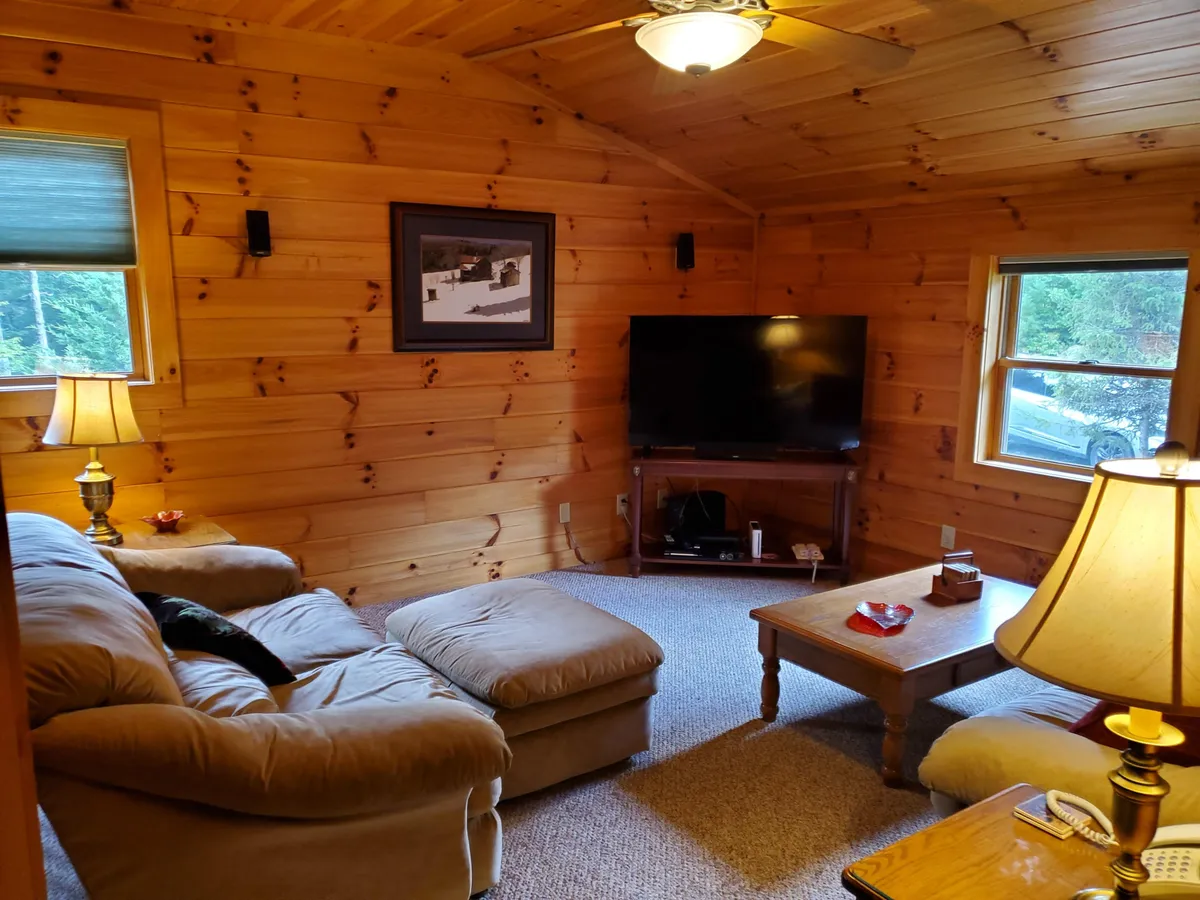 This inviting interior showcases a comfortable sectional sofa, a wooden coffee table, and a large television, bathed in warm light from a lamp. The space is clearly designed for relaxation, group gatherings, and immersive movie watching experiences.