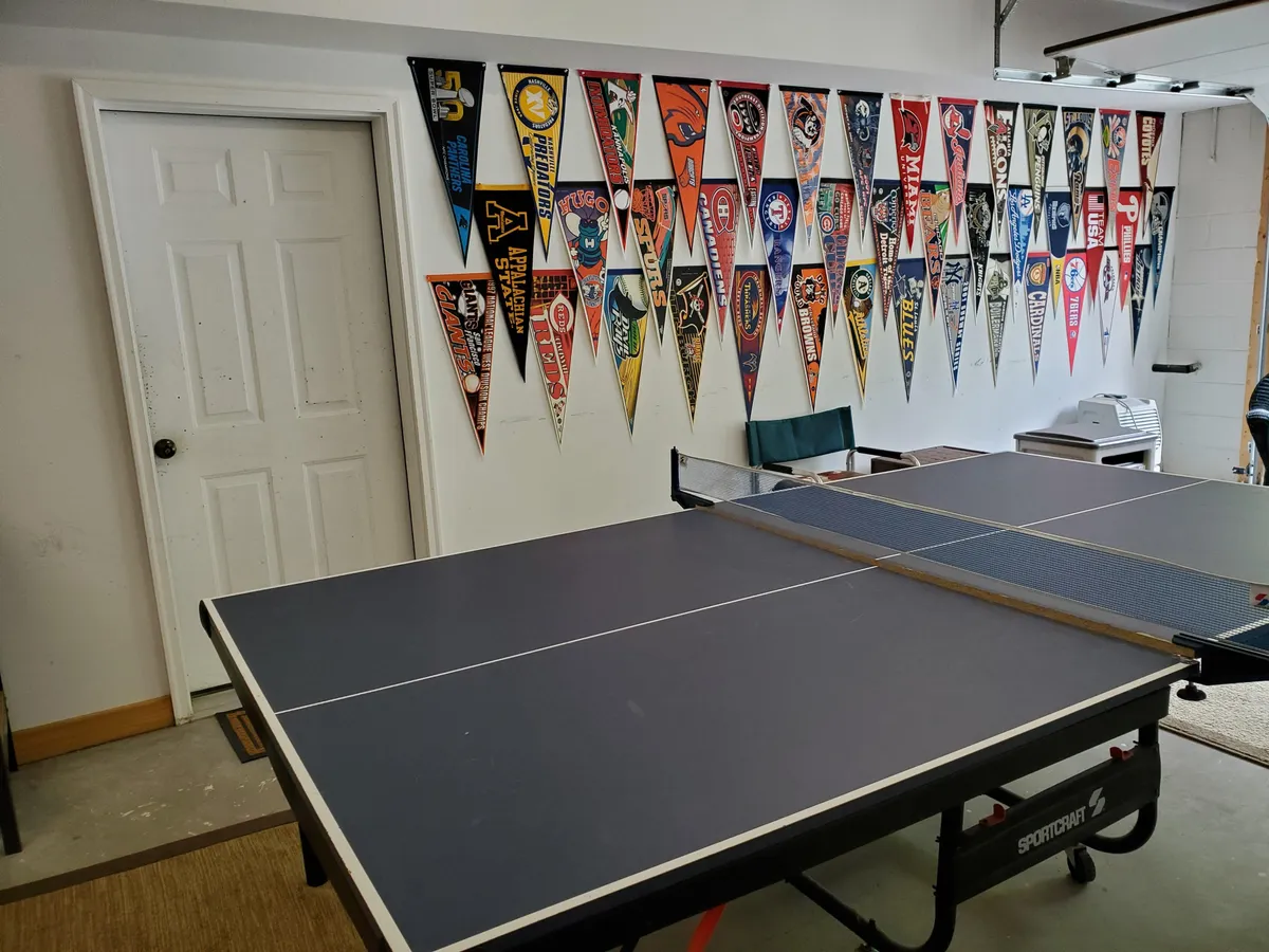A ping pong table takes center stage in this lively interior, with fun pennants on the wall and a bright, open doorway suggesting an energetic, active environment. The space feels dedicated to group activities, making it ideal for competitive play and casual hangouts.