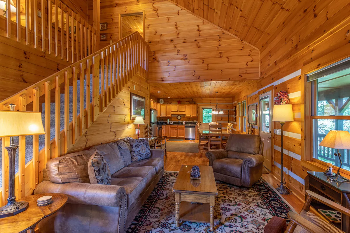 A spacious, inviting open-plan area featuring a sofa, recliner, coffee table, and visible kitchen space. The large kitchen and dining area are ideal for group meals, and the seating arrangement around the coffee table suggests a perfect spot for games and conversation.