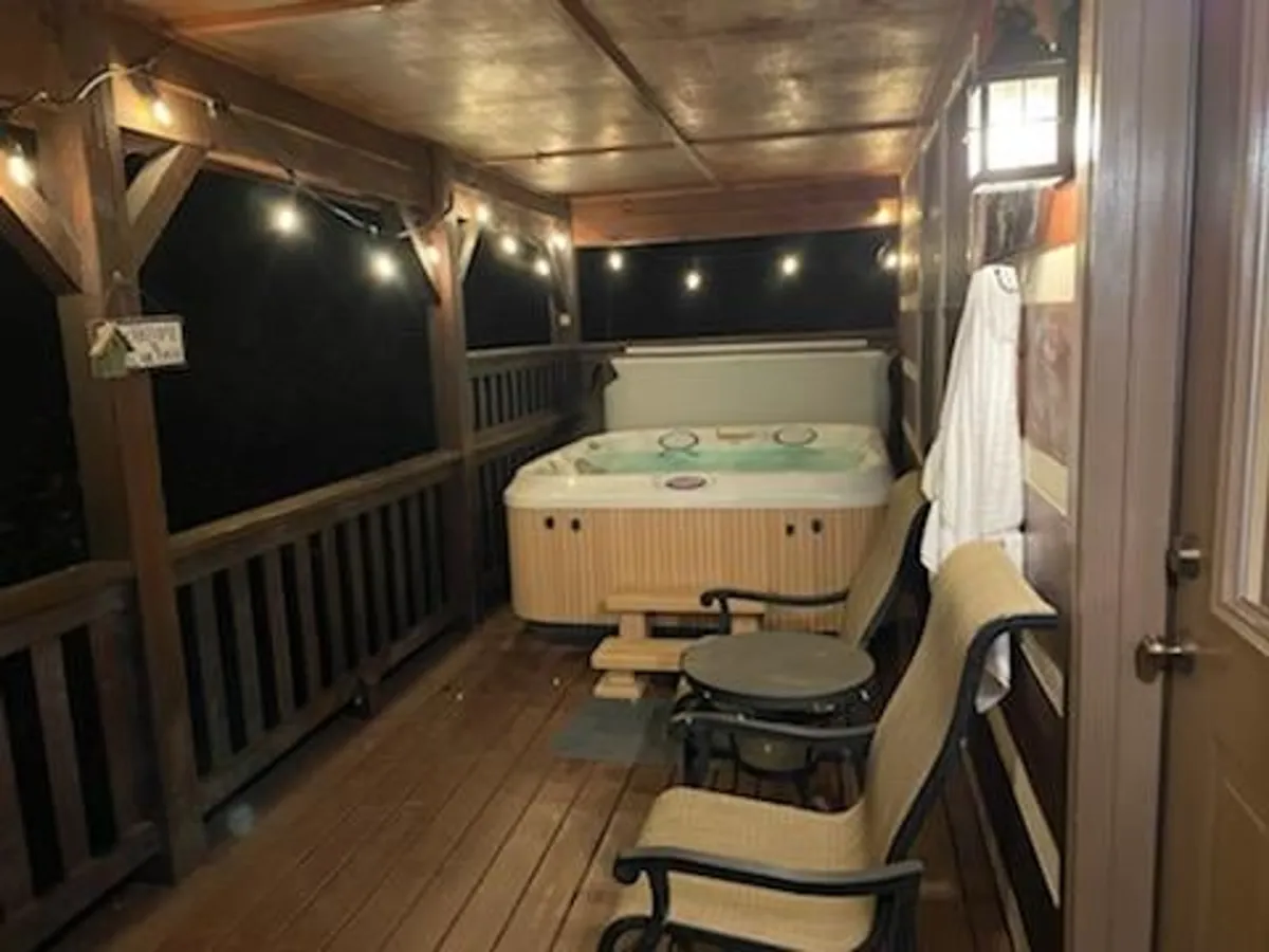 This image shows a cozy hot tub setup on an outdoor deck surrounded by hanging string lights and comfortable seating. The ambiance suggests evenings spent stargazing or sharing stories in a tranquil mountain setting.